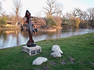 Pohľad na mlyn z brehu, v popredí drevená ryba, ktorá podľa legendy plní želania (Slovensko)